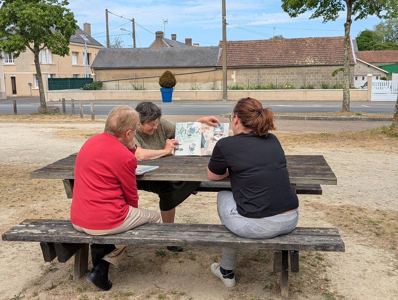 Extérieur, trois femmes lisent des albums sur une tabl de pique-nique et rigolent