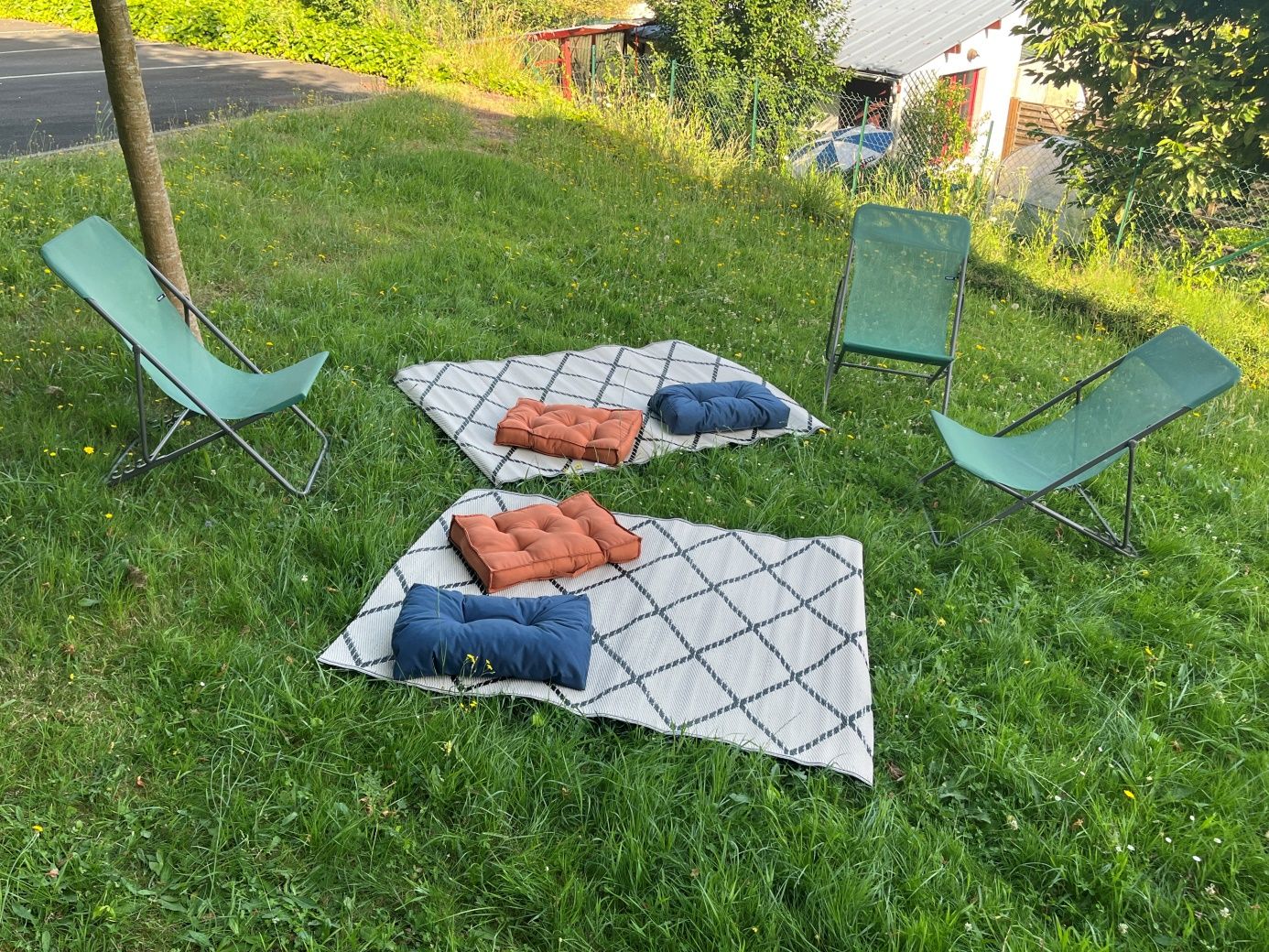 Sur une pelouse sont installés deux tapis, 3 transats et 4 coussins