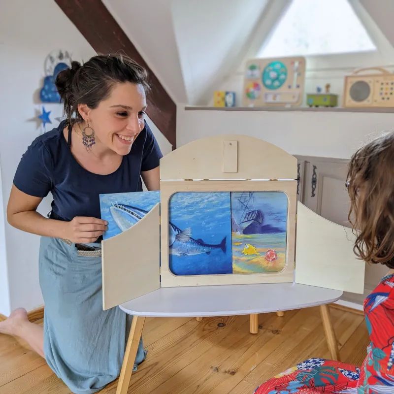 Une femme utilisant un kamishibaï devant un enfant